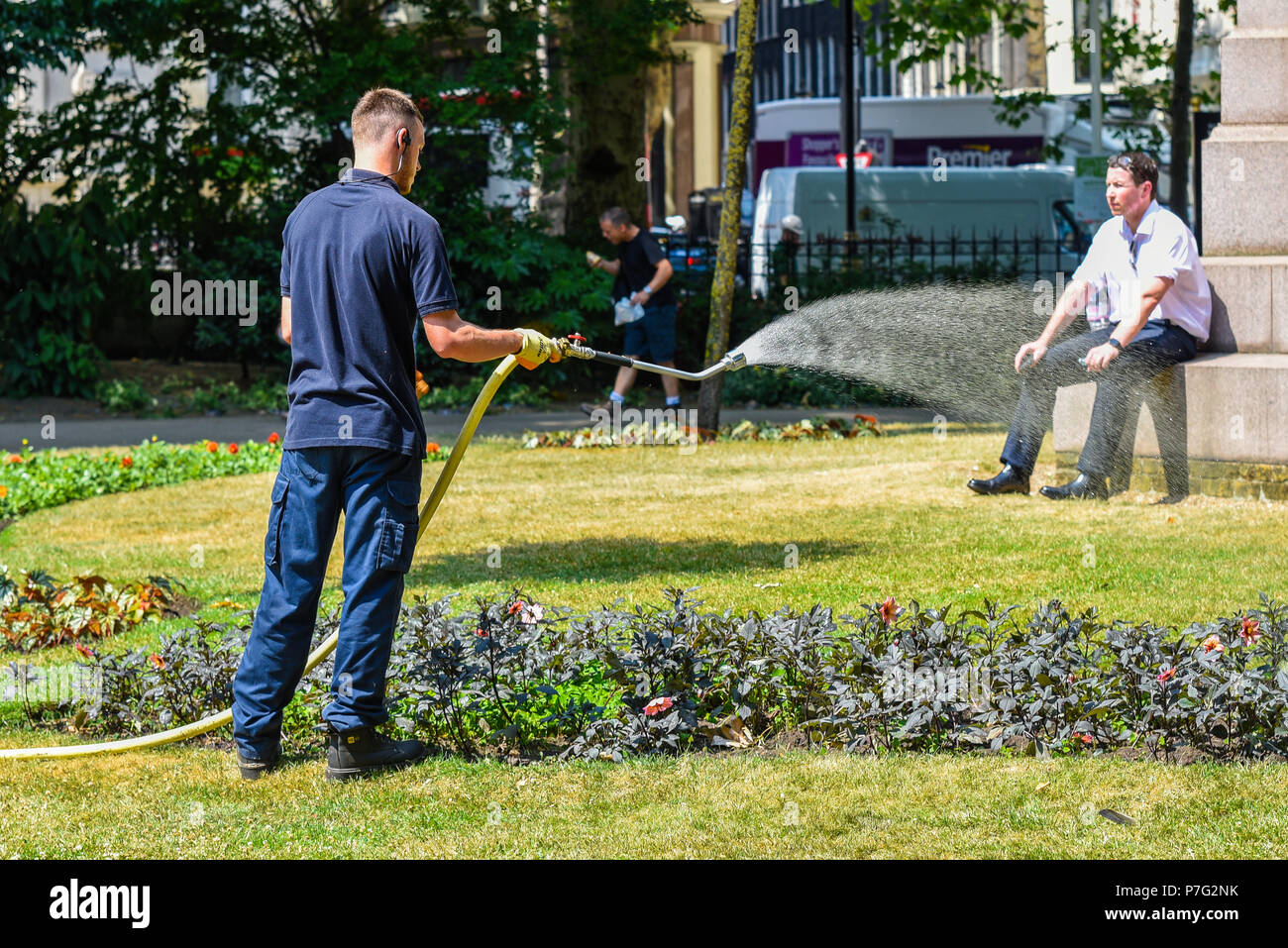 Victoria Embankment Gardens, Londres. Un jardinier arrose les plantes dans les jardins tandis qu'un employé de bureau peut être l'espoir d'une douche Banque D'Images