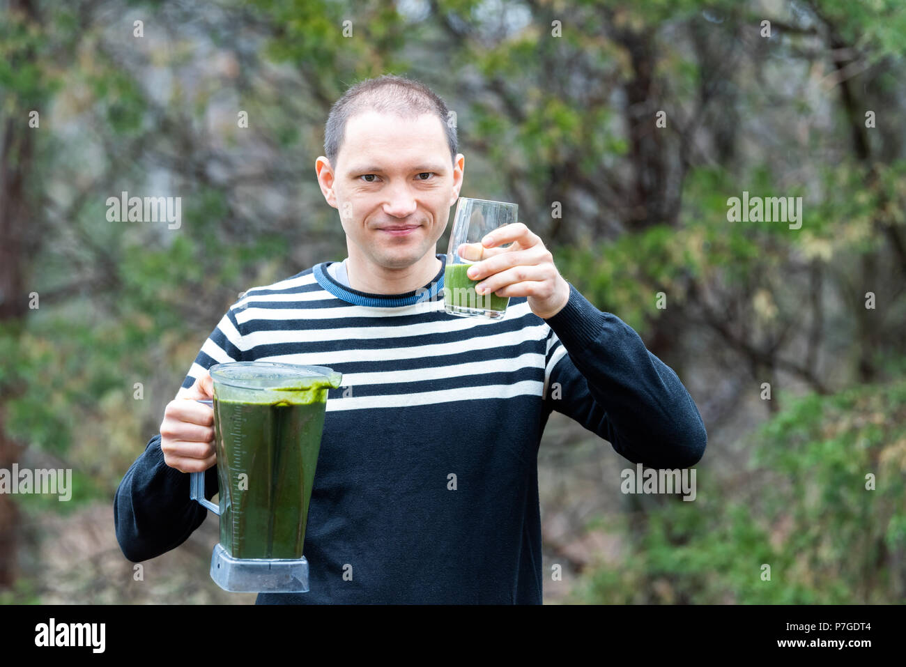 Jeune homme debout à l'extérieur, en plein air, holding plastic contenant du mélangeur, le verre avec smoothie vert fabriqué à partir de légumes verts, Banque D'Images