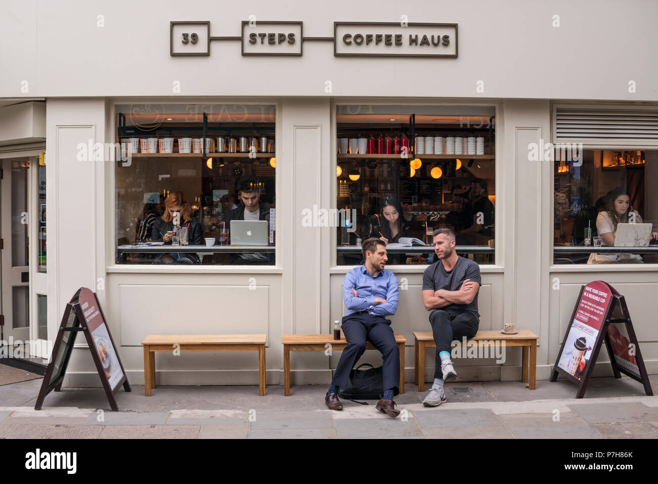 Deux amis assis et parler sur banc en bois à l'extérieur de 39 Étapes Haus Café, London, UK Banque D'Images