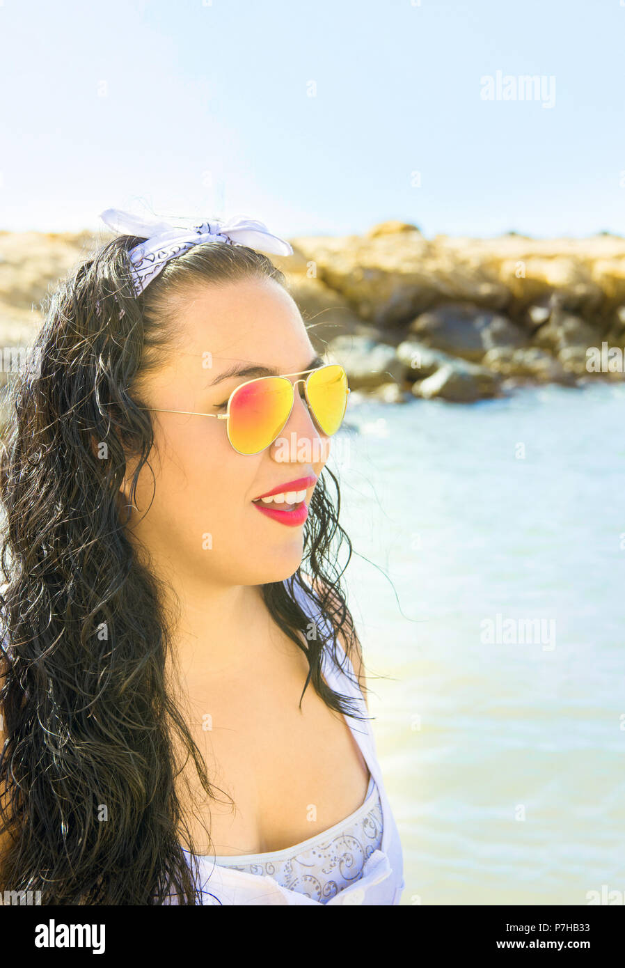 Belle Jeune femme Brune avec de longs cheveux bouclés en lunettes miroir  coloré robe blanche se dresse sur plage mer Smiling rire. Plein Soleil Vi  Photo Stock - Alamy