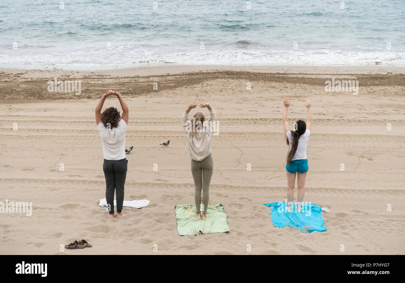 Trois jeunes (deux femmes et un homme) performing Yoga avec pigeons sur la plage Banque D'Images