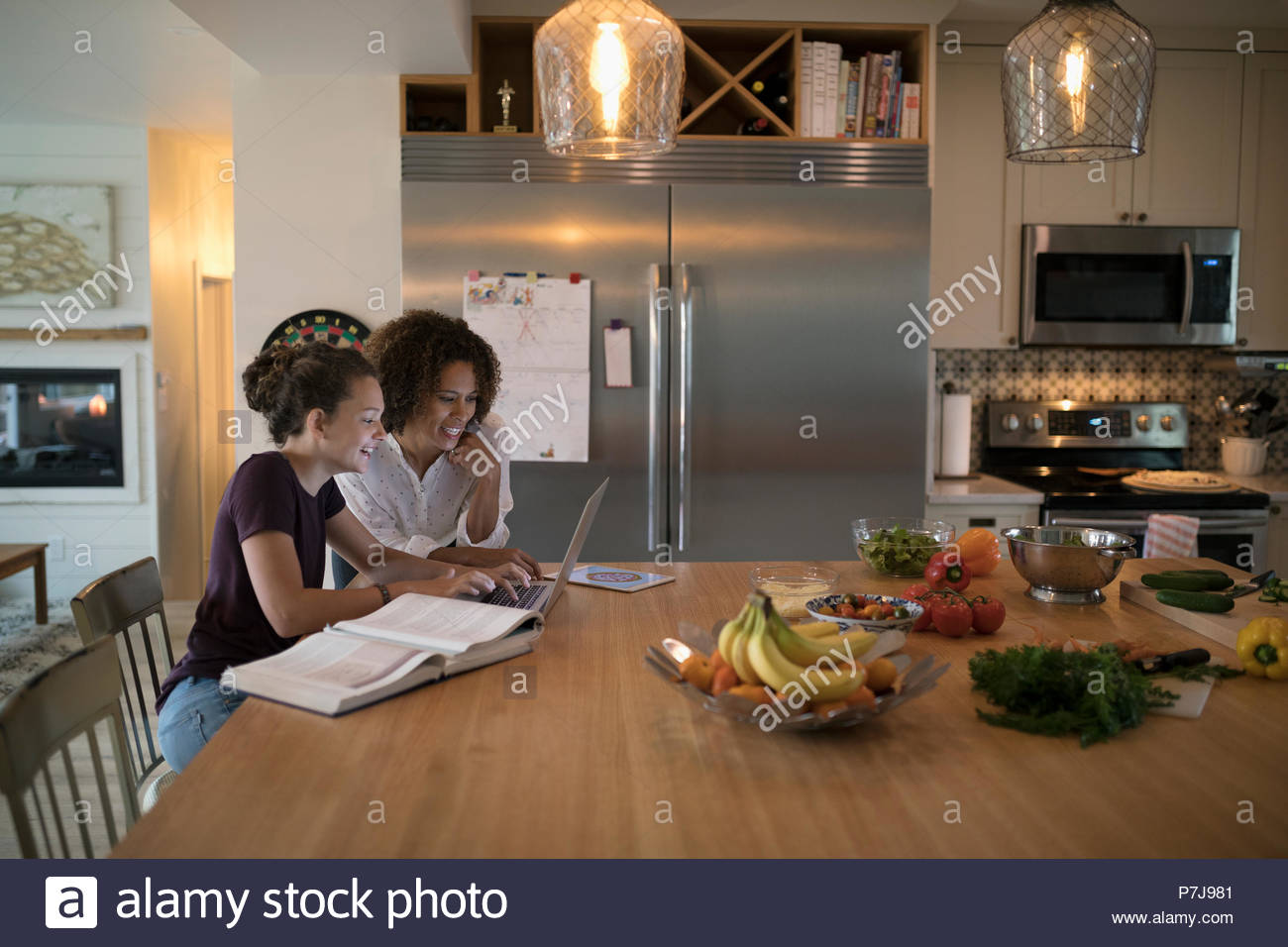 Fille mère aidant à faire leurs devoirs à l'interpolation de l'ordinateur portable dans la cuisine Banque D'Images