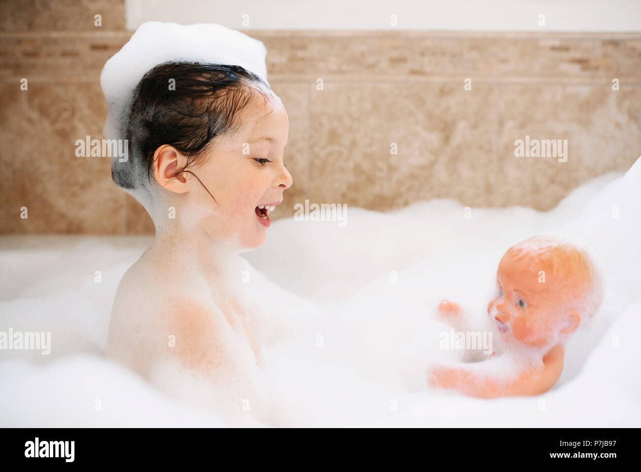 Fille assise dans un bain jouant avec sa poupée Banque D'Images