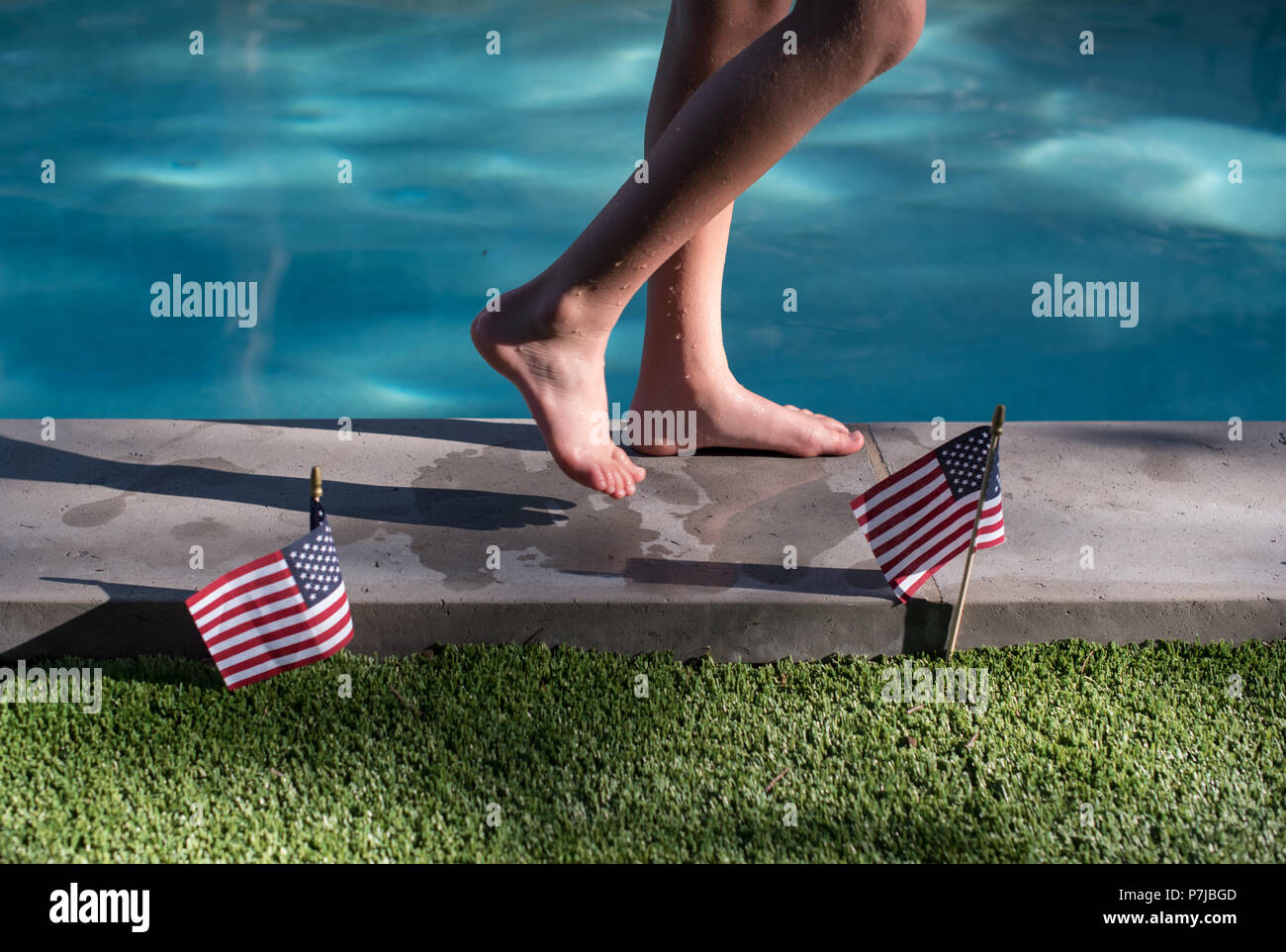 Garçon marchant le long du bord d'une piscine extérieure et d'American flags Banque D'Images