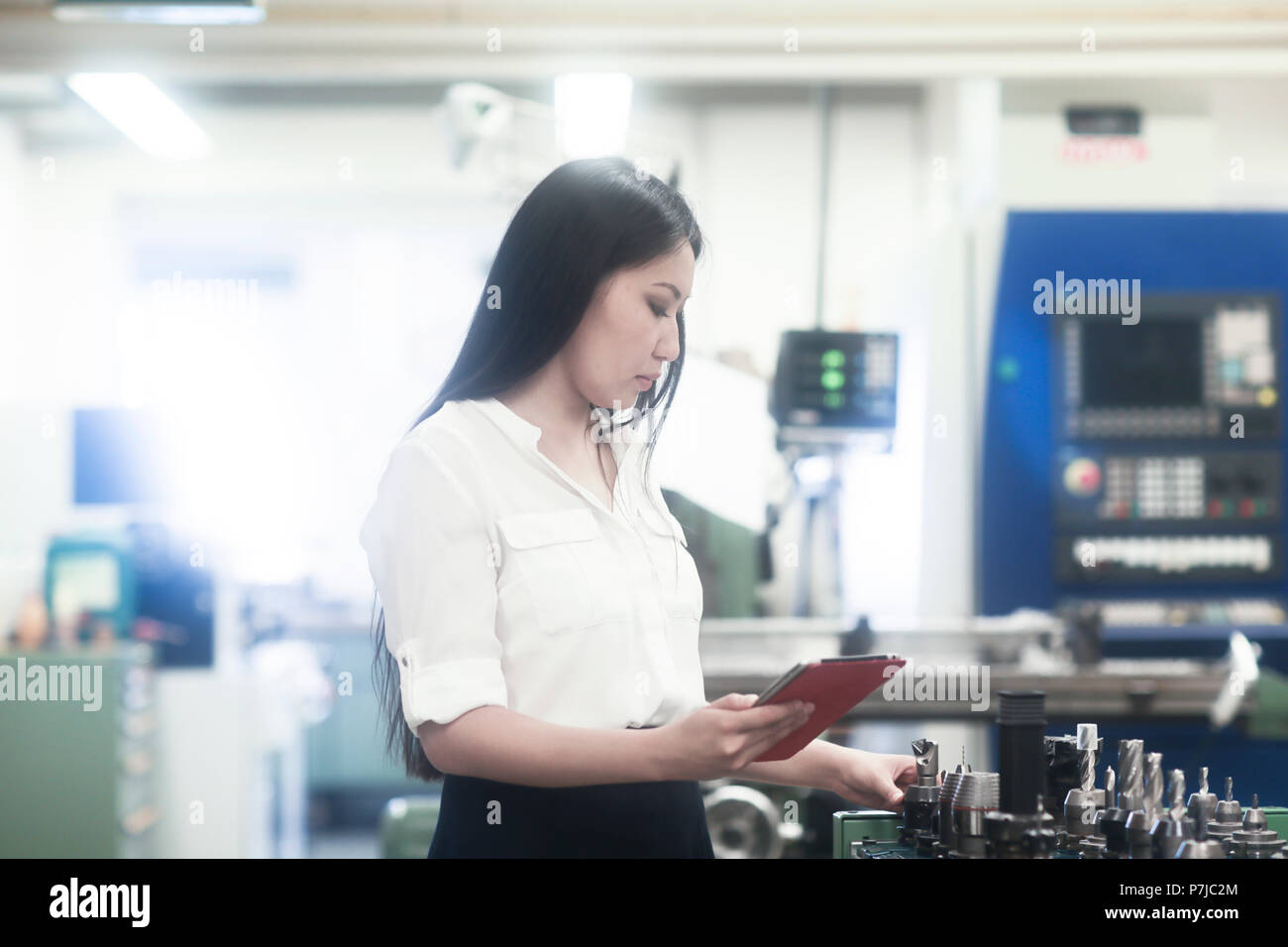 Ingénieur femme debout dans un atelier tenant une tablette numérique et la sélection d'outils de forage Banque D'Images
