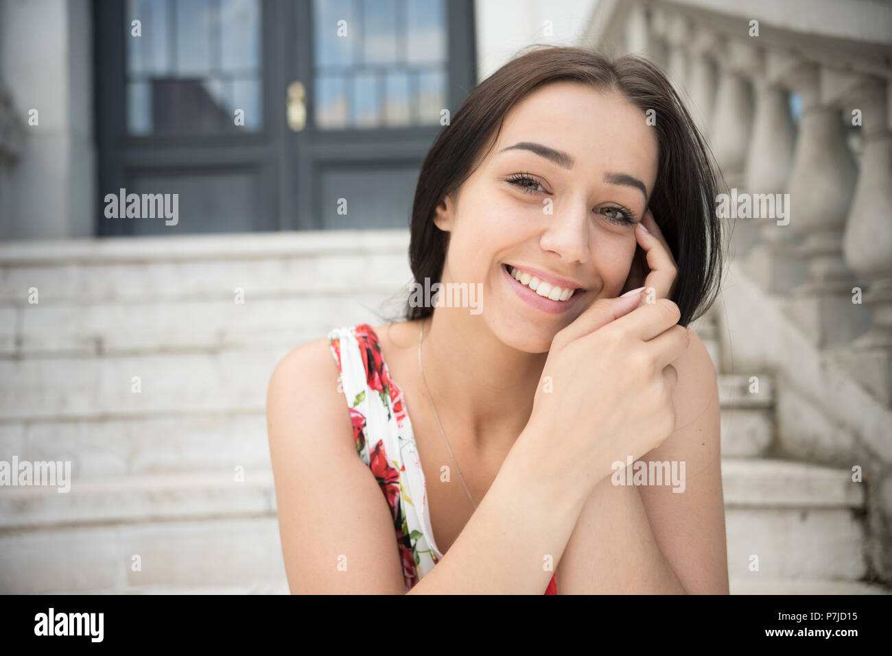 Portrait of a smiling woman sitting on steps à l'extérieur d'un bâtiment Banque D'Images