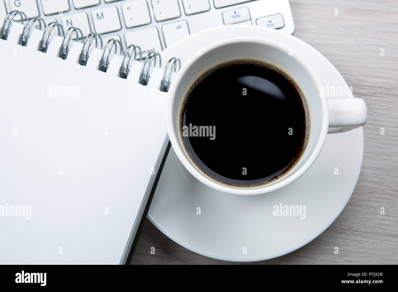 Tasse de café noir blanc avec mousse, bloc-notes, le clavier sur le bureau close up Banque D'Images