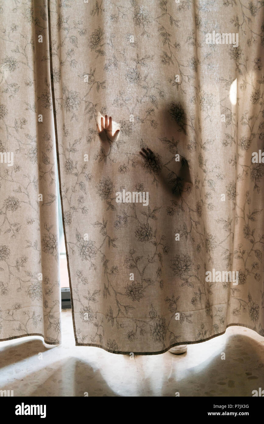 Enfant jouant à cache derrière un rideau, à travers lequel vous pouvez voir sa silhouette. Banque D'Images