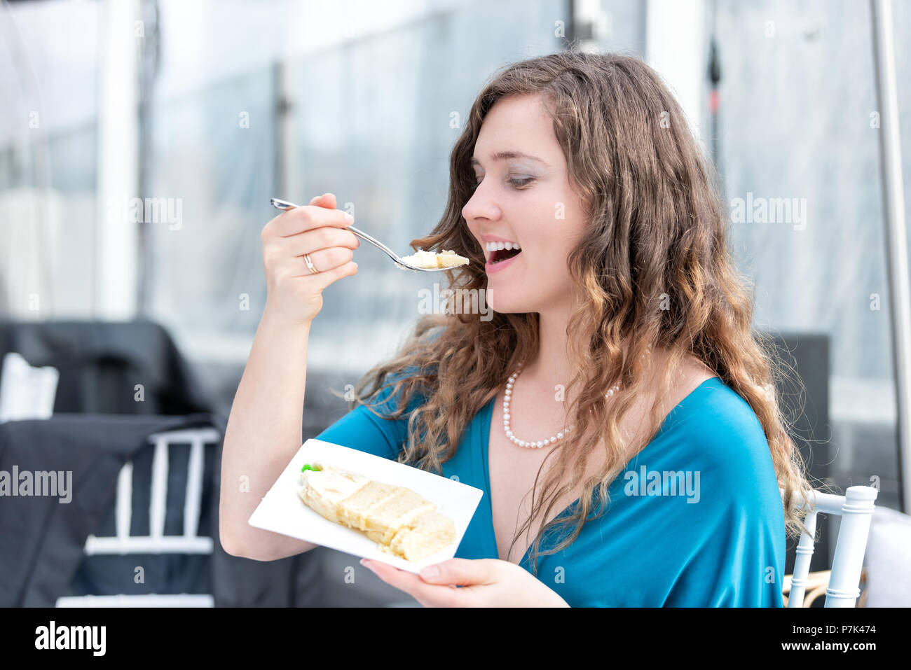 Élégant jeune smiling happy woman eating cake, bouche ouverte avec profil latéral fourche à réception de mariage dessert dîner, sitting at table Banque D'Images