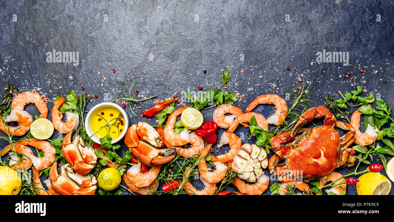 Produits frais et de fruits de mer crus - crevettes et crabes avec des herbes et épices sur fond gris foncé. Copier l'espace. Banque D'Images