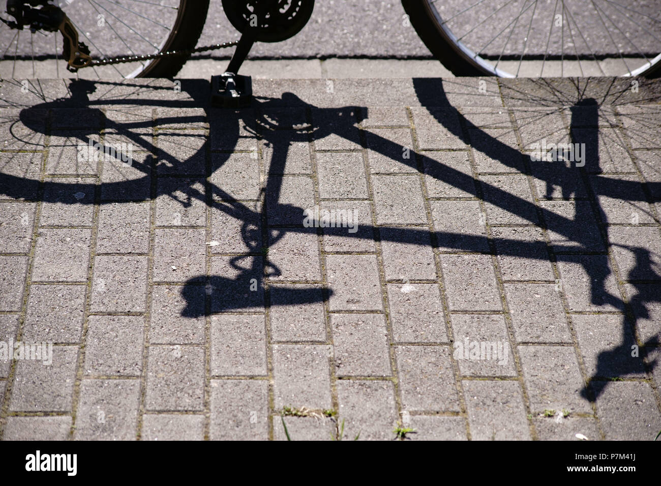 Un vélo en stationnement jette une ombre sur le trottoir. Banque D'Images