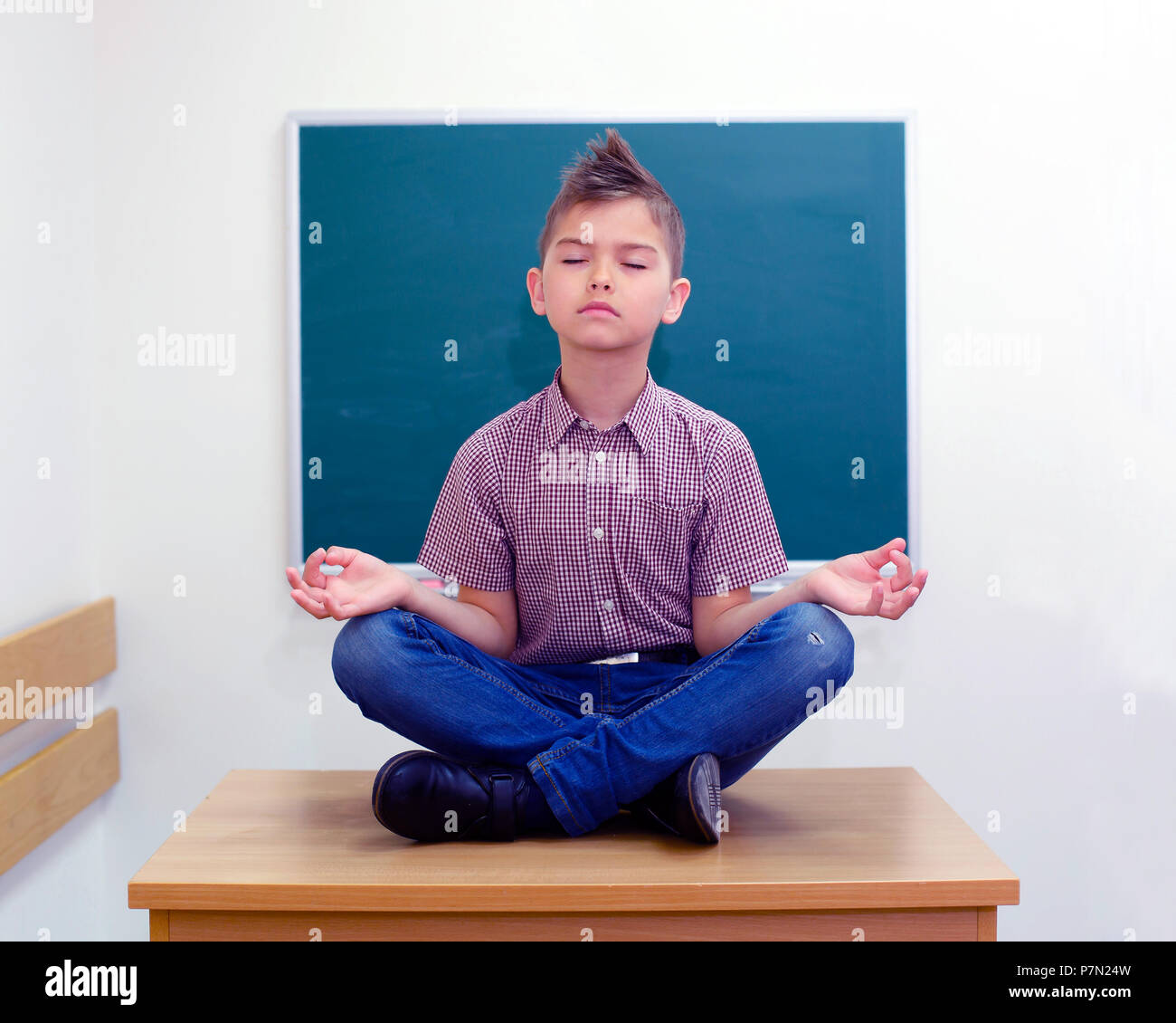 Collégien dans un lotus posent la méditation et le yoga assis à l'école sur la table. Banque D'Images
