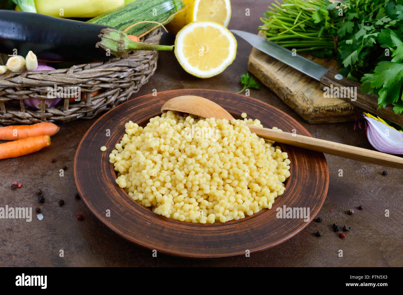 Couscous délicieux porridge utile dans une plaque d'argile et de matières premières dans un panier de légumes frais, verts, citron. Ingrédients pour cuisiner un taboulé. Des plats végétariens Banque D'Images