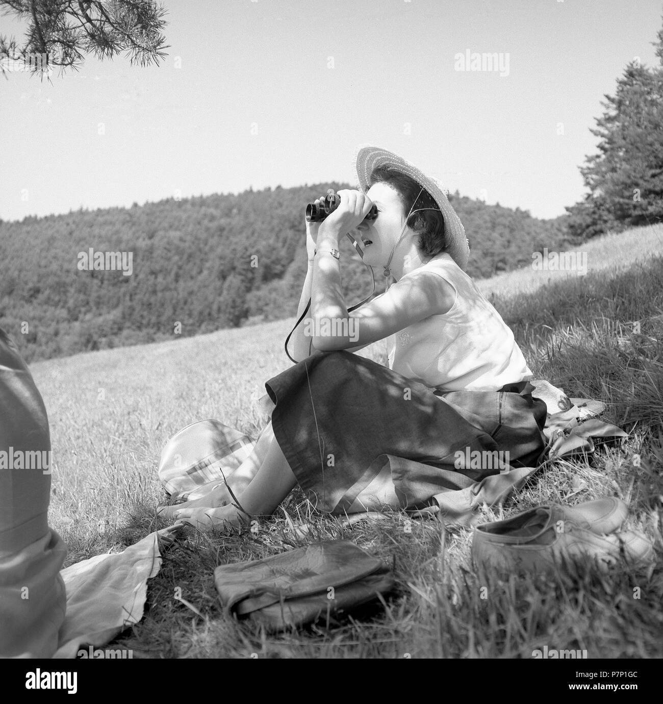 Femme assise dans la nature à la recherche dans les jumelles autour de 1950, près de Fribourg, Allemagne Banque D'Images