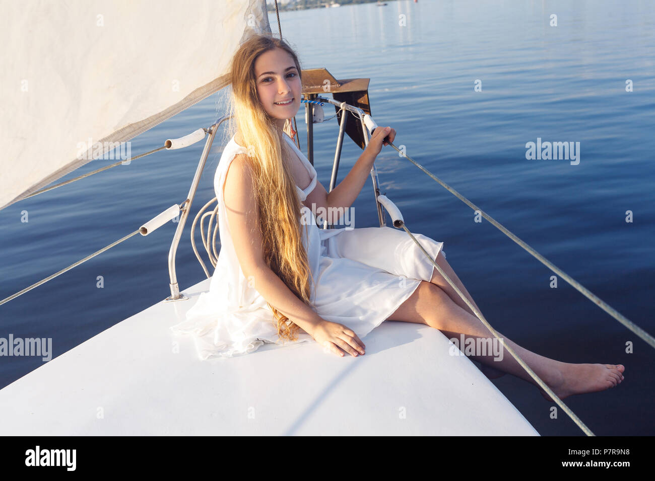 Portrait of happy smiley dentelée jolie fille avec robe blanche et long cheveux blonds debout sur yacht en été. Vue de dessus et à la séance. Banque D'Images