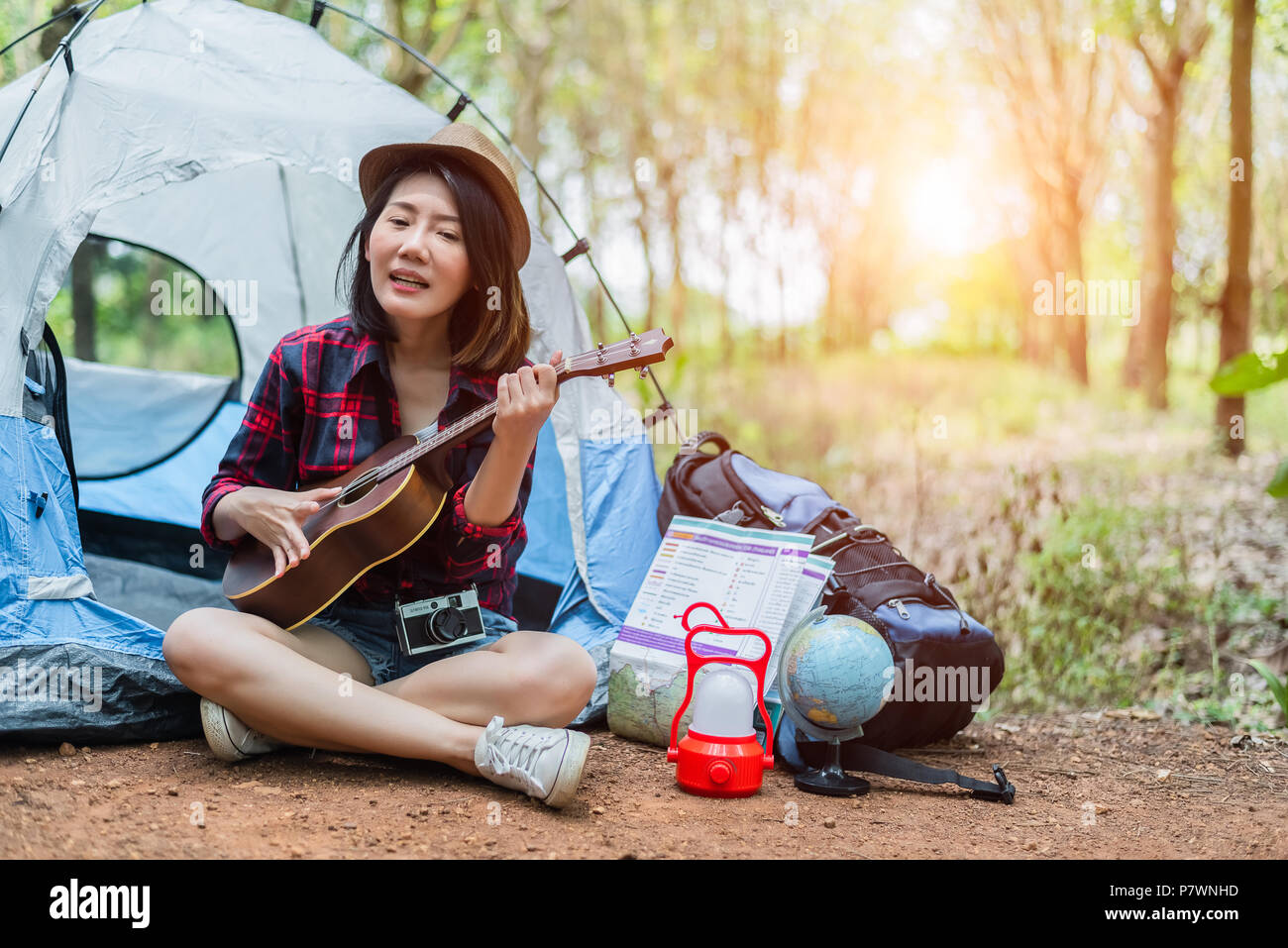 Belle asiatique femme jouant de ukulele en face de tente de camping dans une forêt de pins. Les gens et les modes de concept. Thème Aventure et de voyage. Banque D'Images