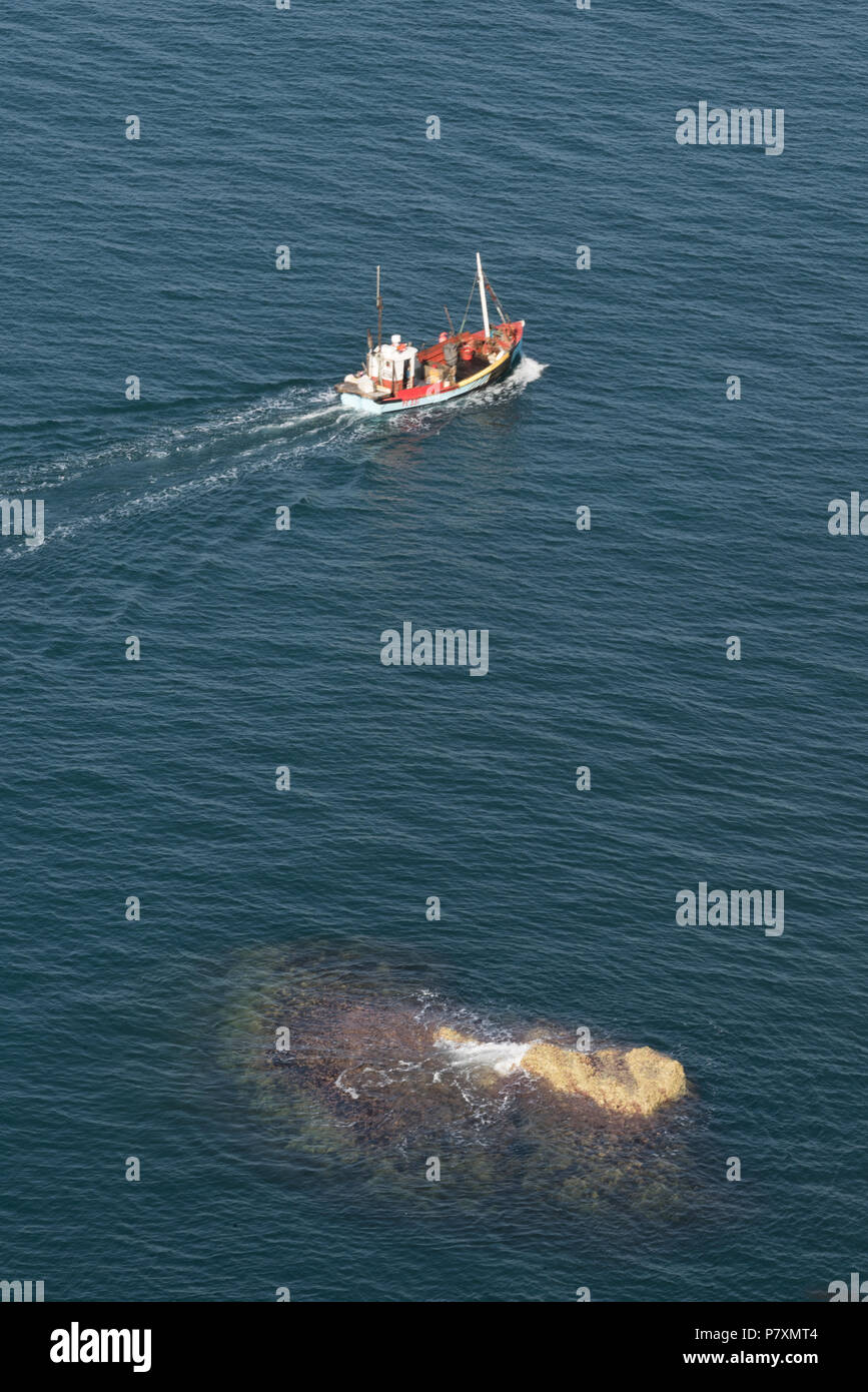 Un petit bateau de pêche côtière en mer en passant un rock submergées. Banque D'Images