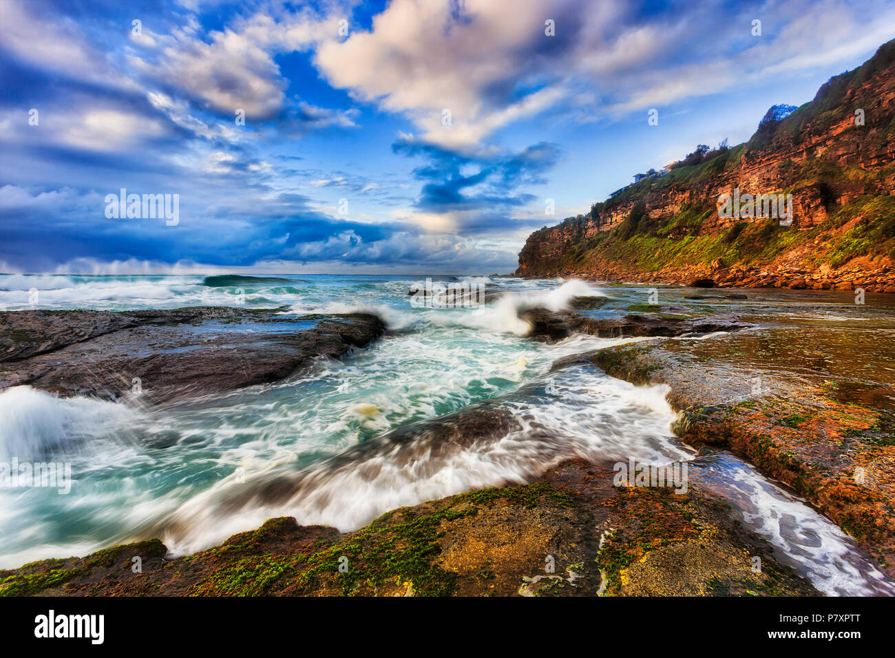 Cloudy stormy matin à bungan beach de cailloux et de roches avec de fortes vagues frapper pointe de grès sur plages du nord de Sydney Australian Banque D'Images