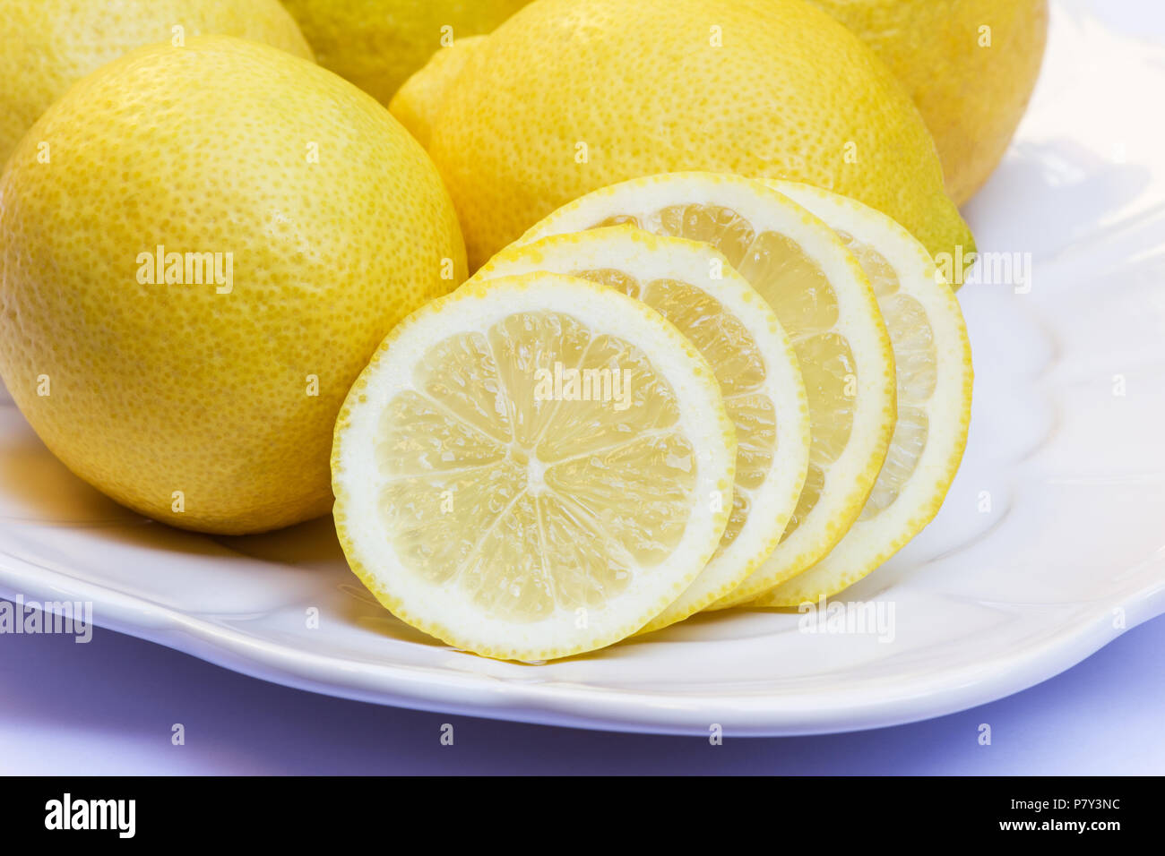 Tranchés et citrons entiers sur un plateau blanc sur fond blanc Banque D'Images