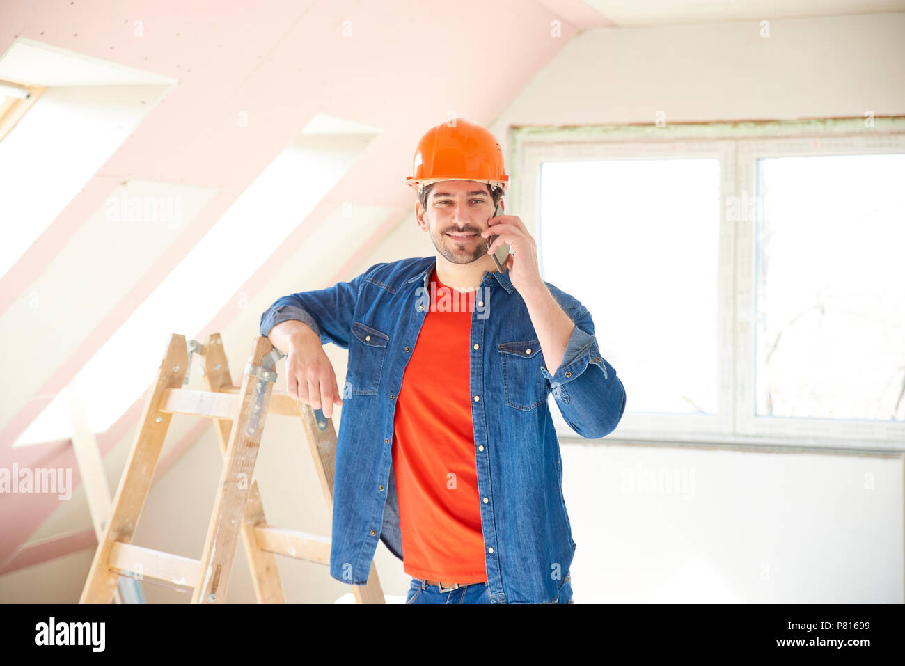 Beau jeune réparateur en utilisant son téléphone portable tout en se tenant dans la chambre et de travailler sur les réparations de l'intérieur. Banque D'Images
