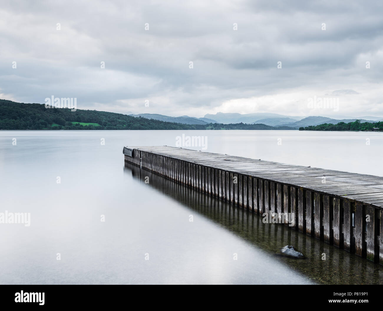Pier s'étend dans les eaux calmes du lac Windermere à Miller la masse dans le Lake District avec les Langdale Pikes dans la distance Banque D'Images