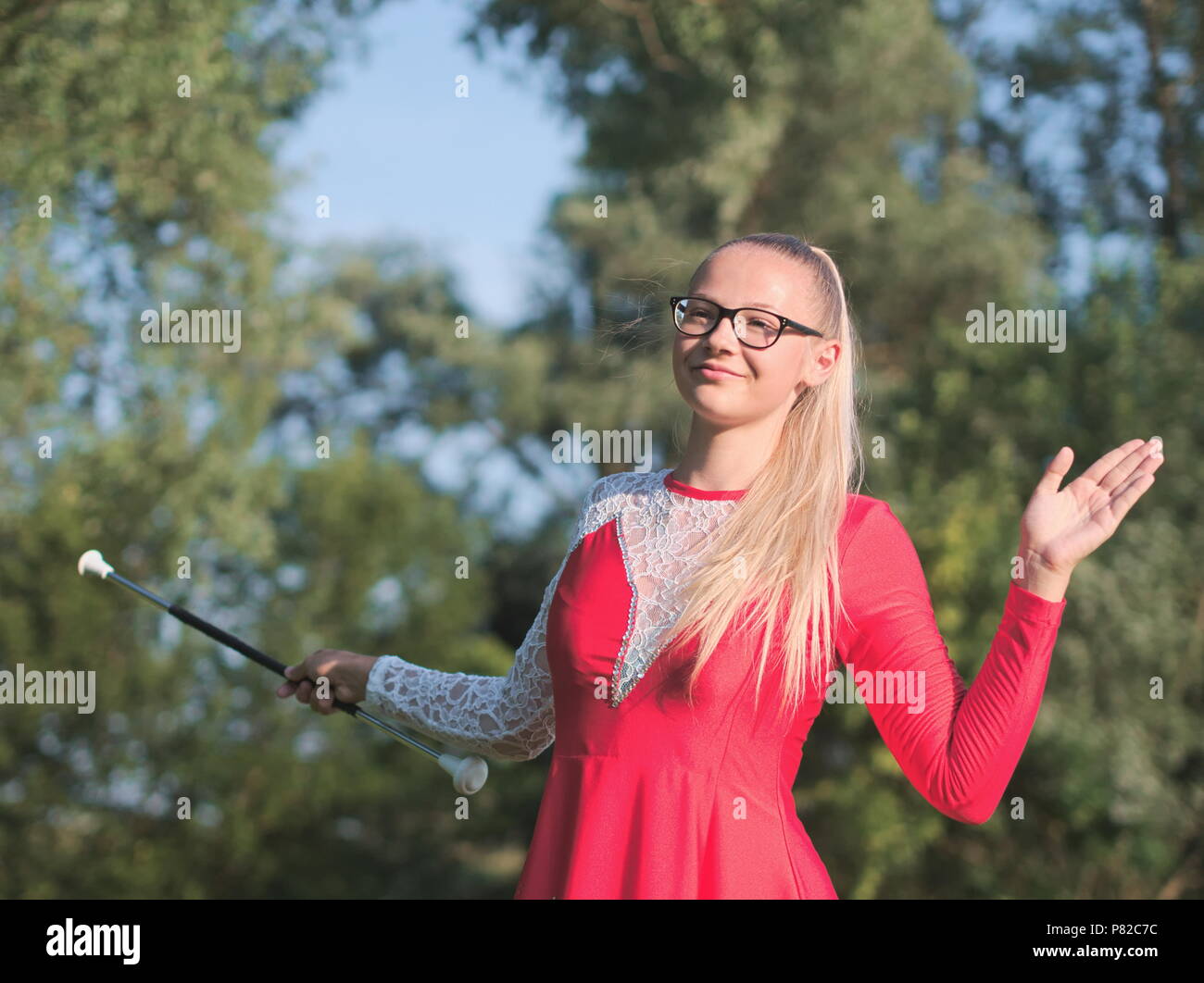 Teen blonde à lunettes fille Majorette Twirling Baton en plein air en robe rouge Banque D'Images