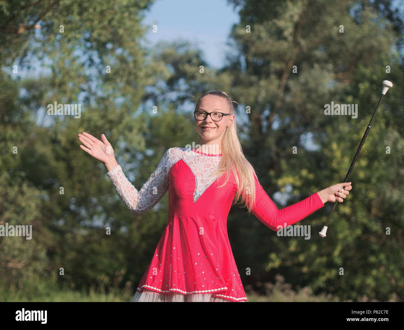 Teen blonde à lunettes fille Majorette Twirling Baton en plein air en robe rouge Banque D'Images