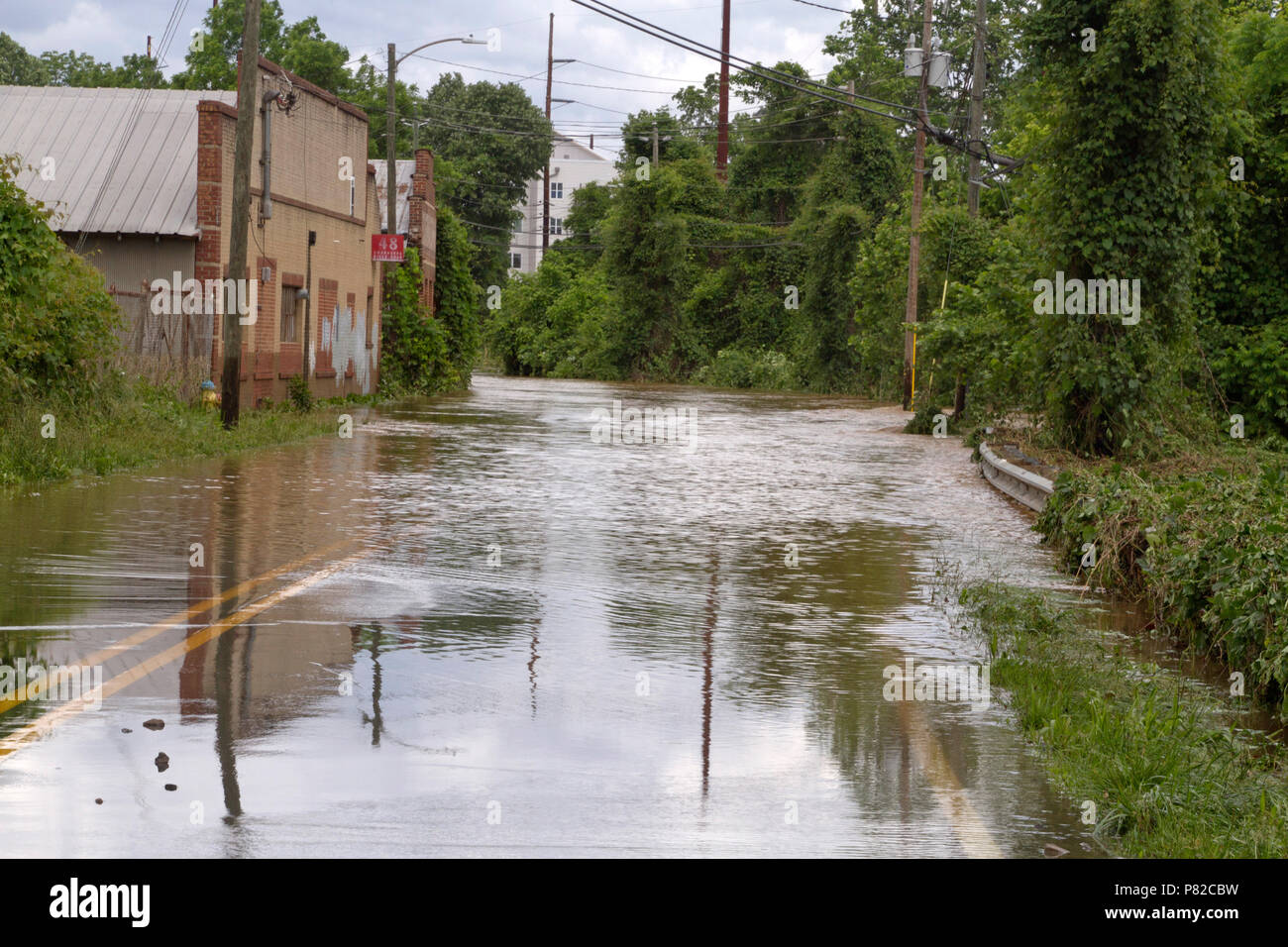 Le haut de l'eau boueuse d'une rivière se déverse sur ses rives après des jours de pluie et les inondations, une étroite route de campagne Banque D'Images