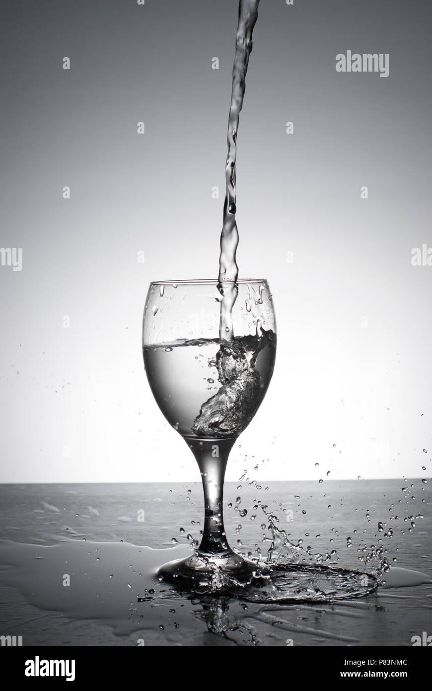 L'eau est versée dans le verre de vin, rétroéclairé sur fond blanc avec des touches.Vitesse d'obturation. Motion gelée. Banque D'Images