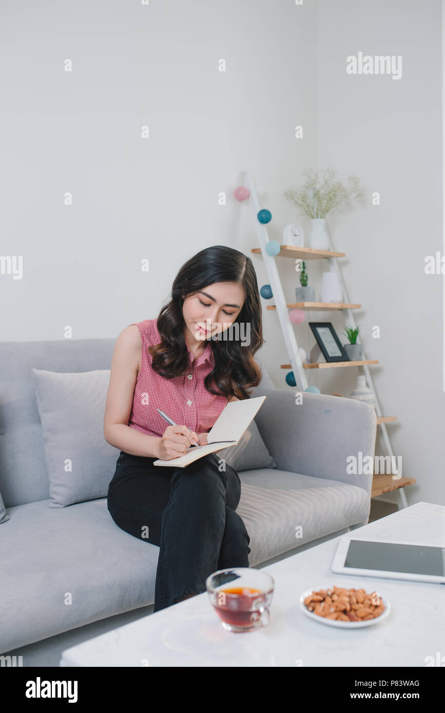 Femme assise à la table, écrit dans l'ordinateur portable et de boire du café à nice light home intérieur. Le travail à domicile. Freelancer. écrire les idées. Banque D'Images