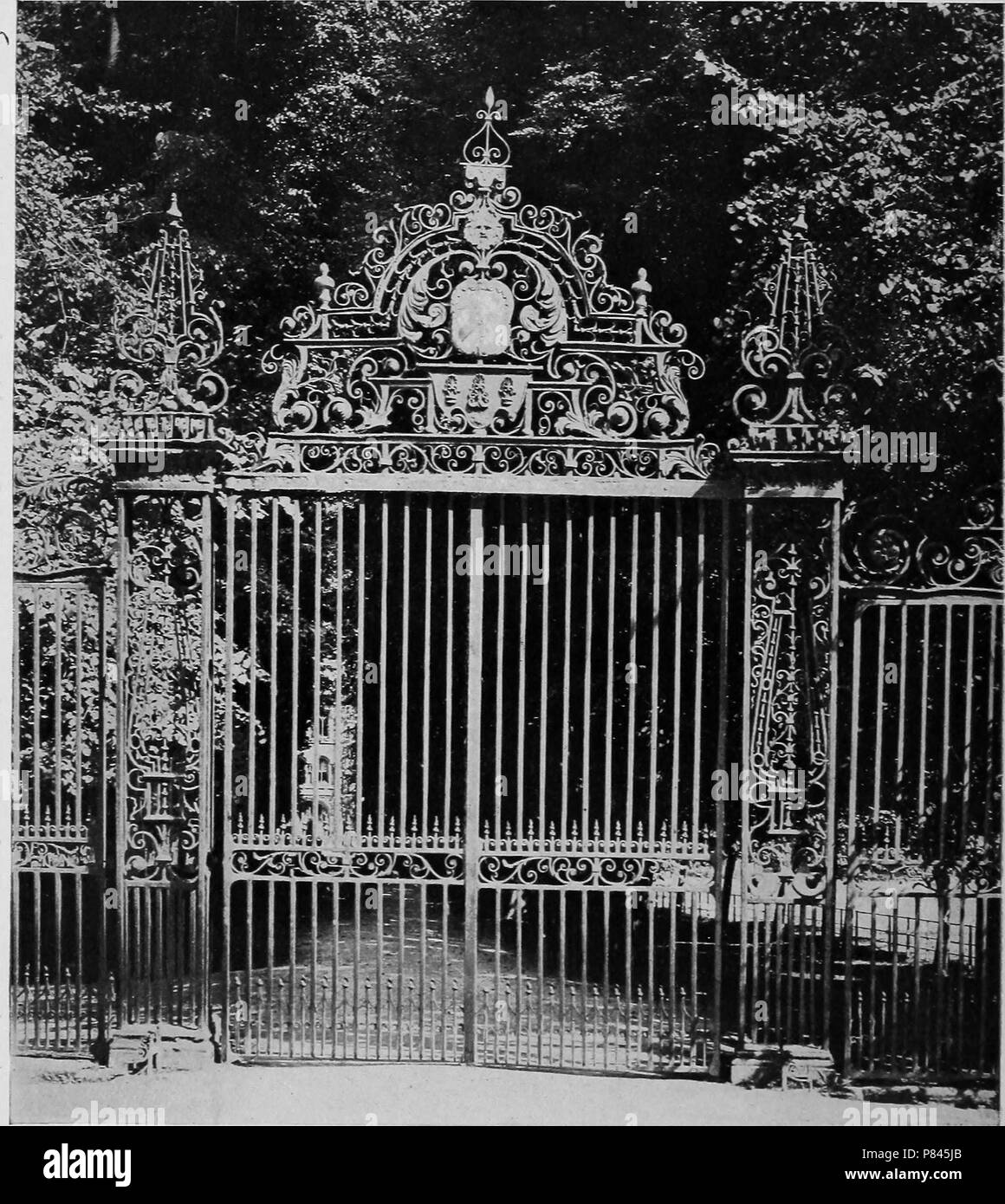 Photographie en noir et blanc représentant un début du xviiie siècle et porte en fer forgé, avec le feuillage en arrière-plan, conduisant à Trinity College de Cambridge, Angleterre, 1922. Avec la permission de Internet Archive. () Banque D'Images