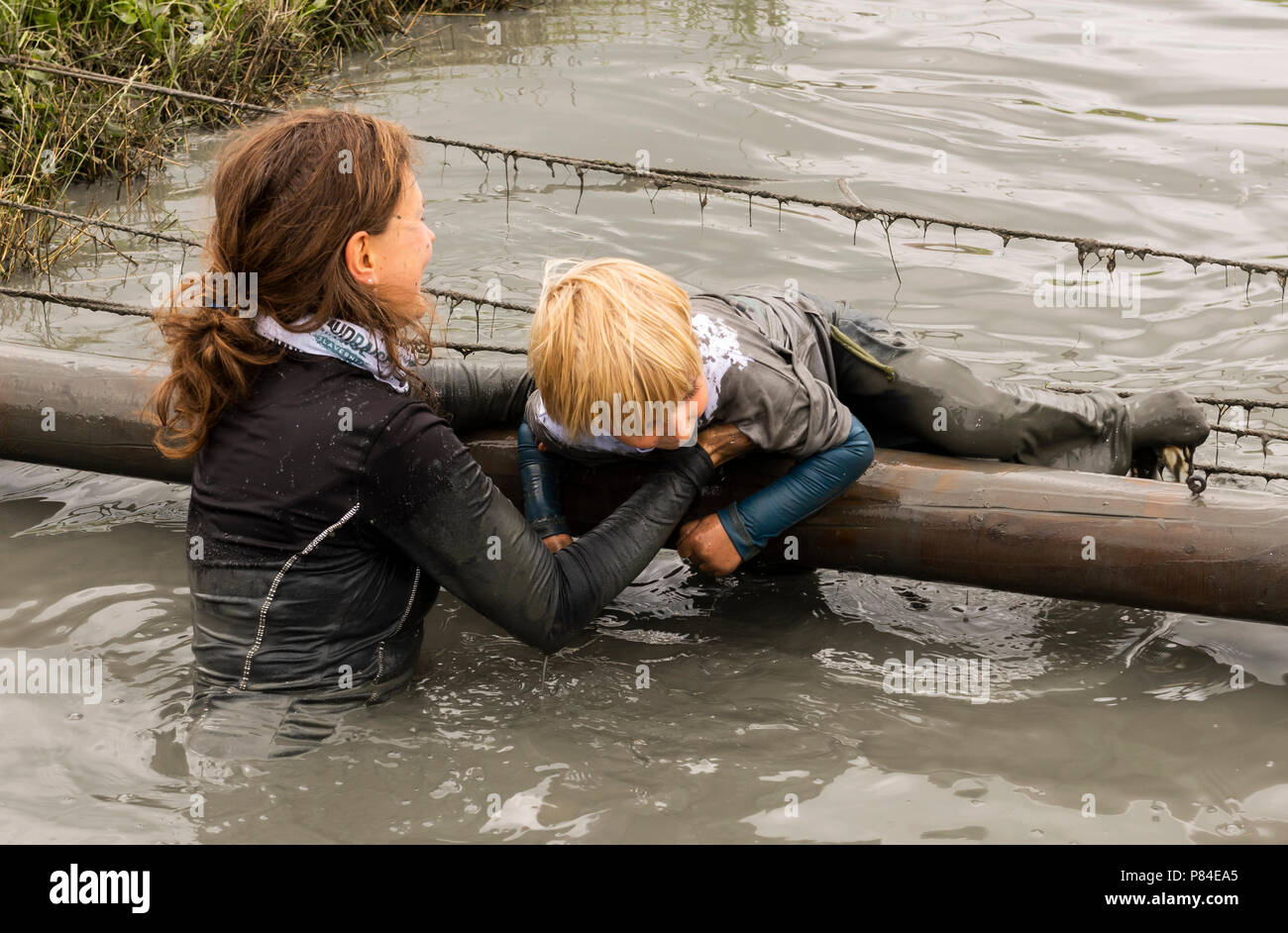 Biddinghuizen, Pays-Bas - le 23 juin 2018 : aider l'enfant pendant un mud run (mudraise) dans la boue et dans l'eau. Banque D'Images