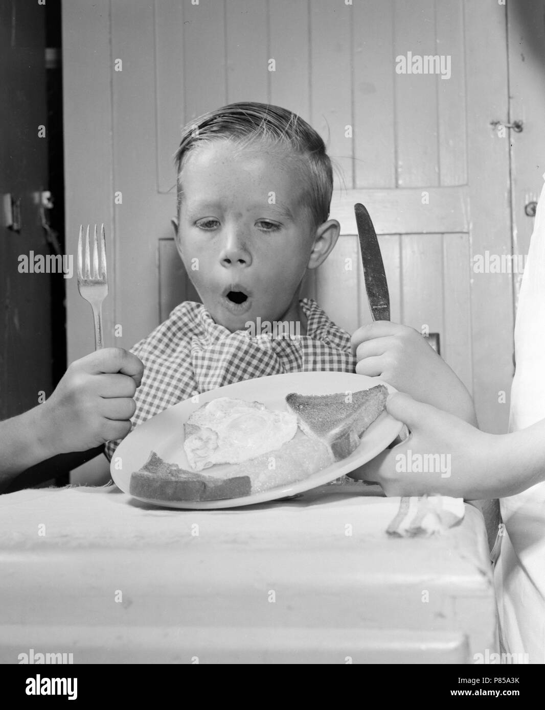 Un jeune garçon est excité par un petit-déjeuner composé de pain grillé et d'œufs, ca. 1955. Banque D'Images