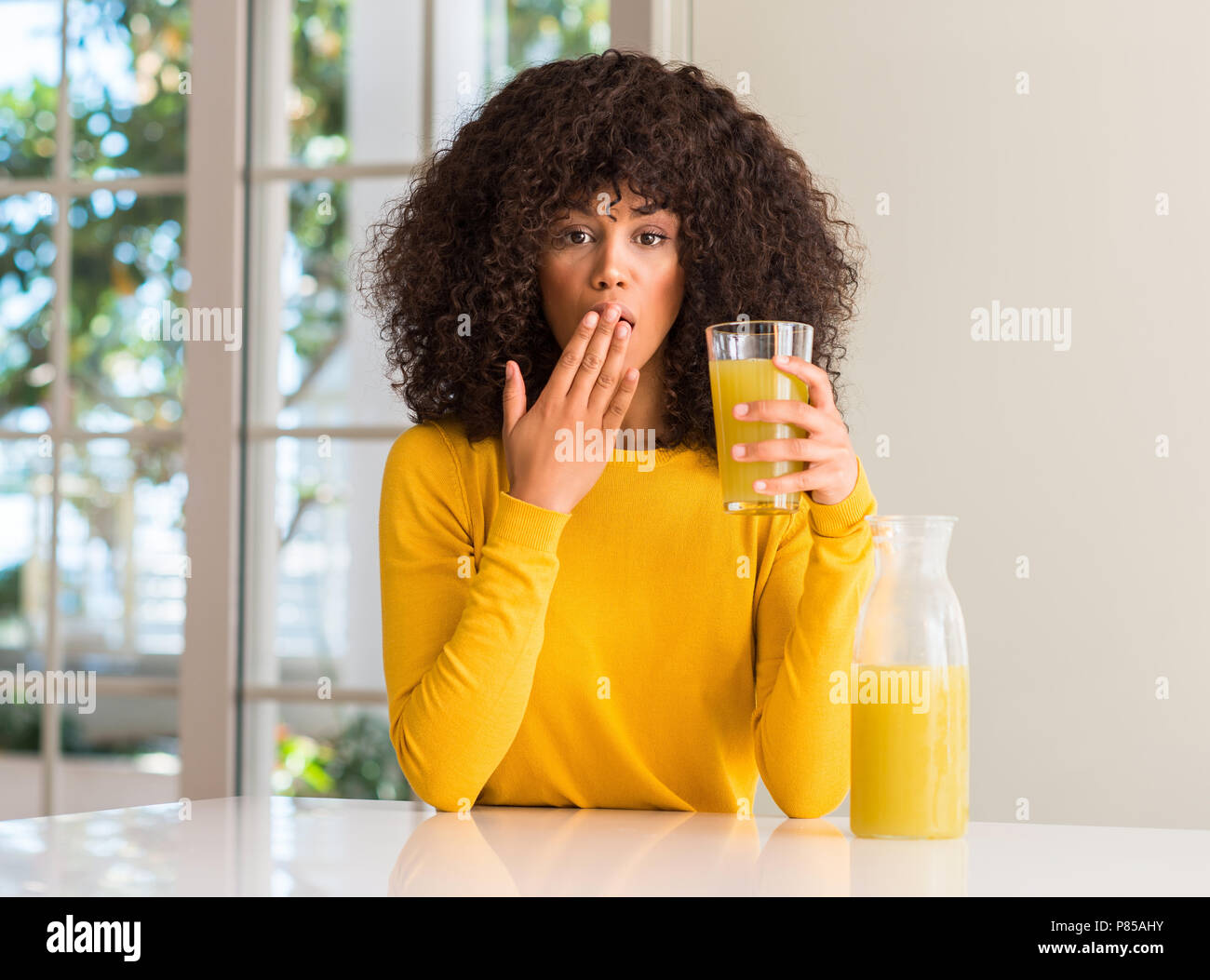 African American Woman boire des jus de fruits sains à couvrir la bouche à part choqué avec honte pour erreur, expression de la peur, peur en silenc Banque D'Images