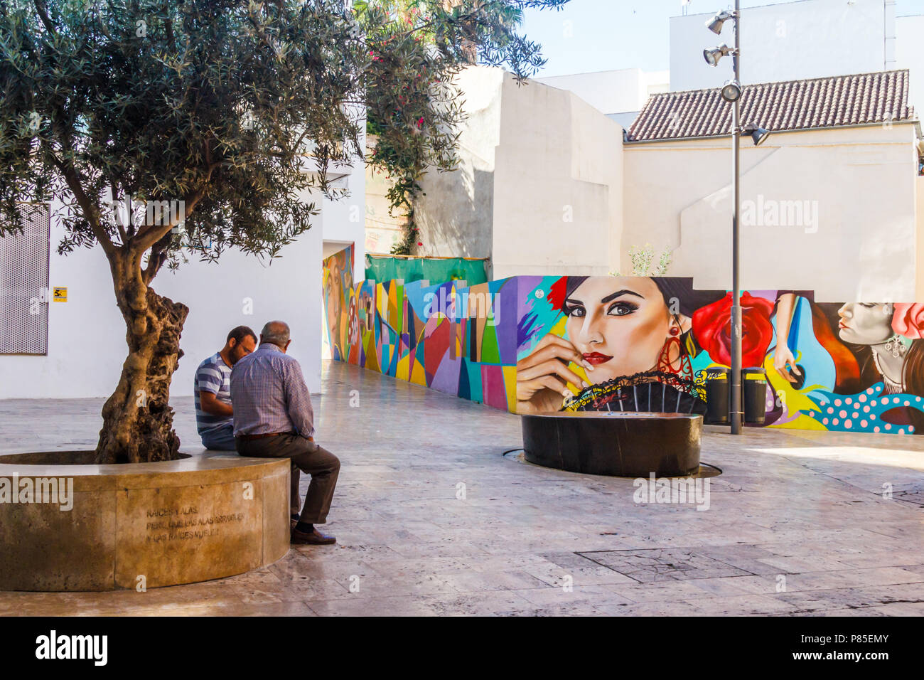 Malaga, Espagne 18 Juin 2018 : deux hommes assis à parler en petit carré avec wall mural. La murale est typiquement espagnol Banque D'Images