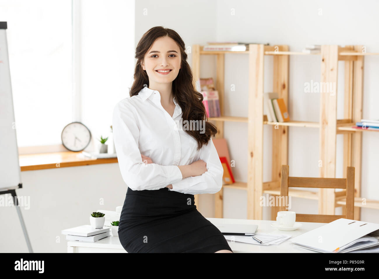 Portrait de jeune belle femme d'affaires dans le bureau. Souriant et bras croisés. Banque D'Images