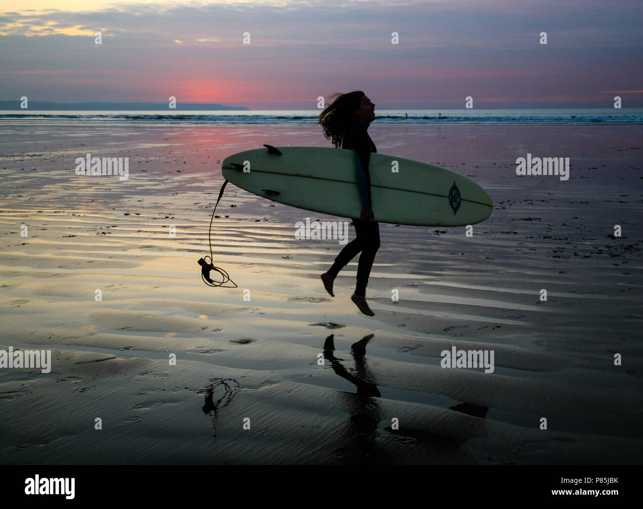 Jeune internaute sauter de joie avec son conseil comme elle partira soir surfant à Westward Ho ! Beach, North Devon, Angleterre, Europe. Banque D'Images