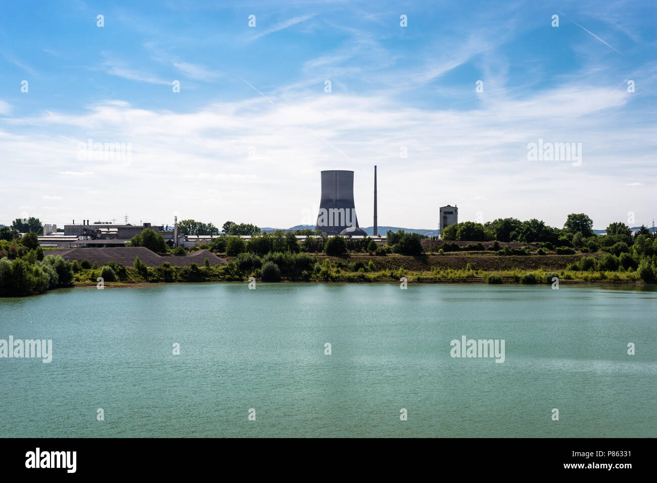 Une énorme cheminée d'une centrale nucléaire dans l'ouest de l'Allemagne, un réservoir d'eau turquoise, un ciel bleu avec des nuages blancs. Banque D'Images