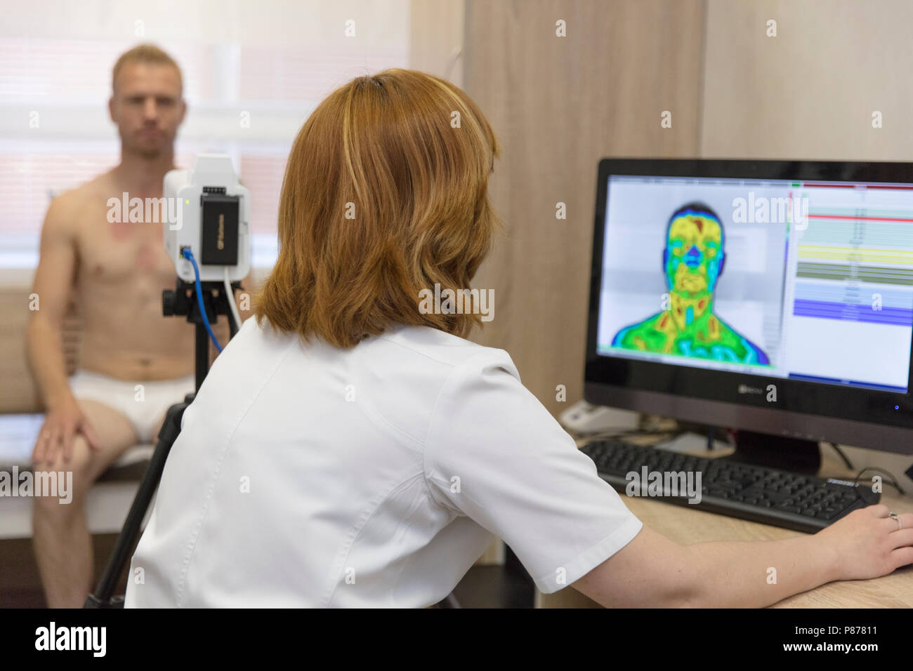 Un jeune homme à la réception d'un médecin sur une étude thermographique avec un imageur thermique de la tête et du cou de l'examen Banque D'Images