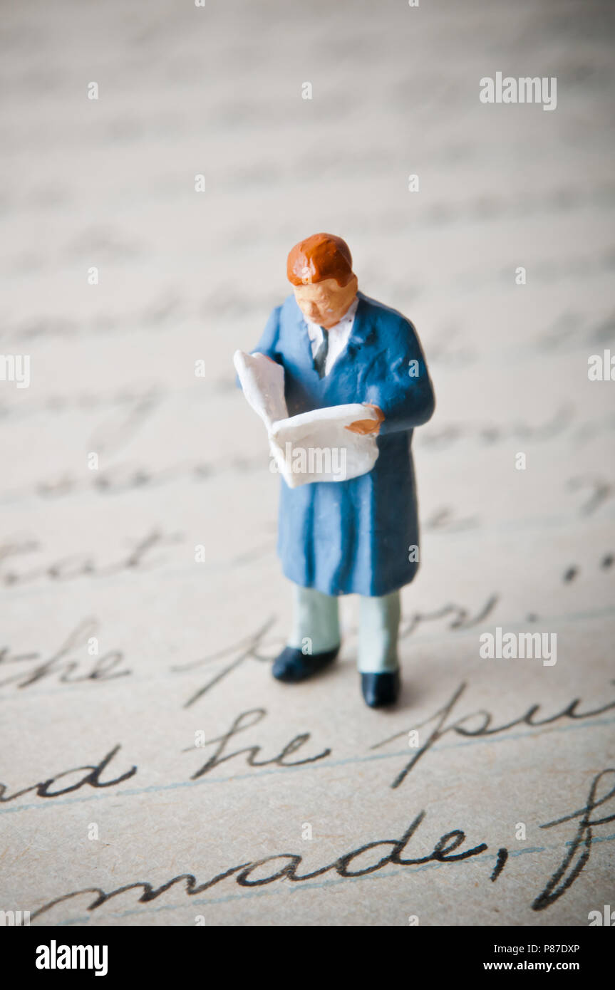 Figurine miniature d'un homme lisant un journal et debout sur une lettre manuscrite Banque D'Images