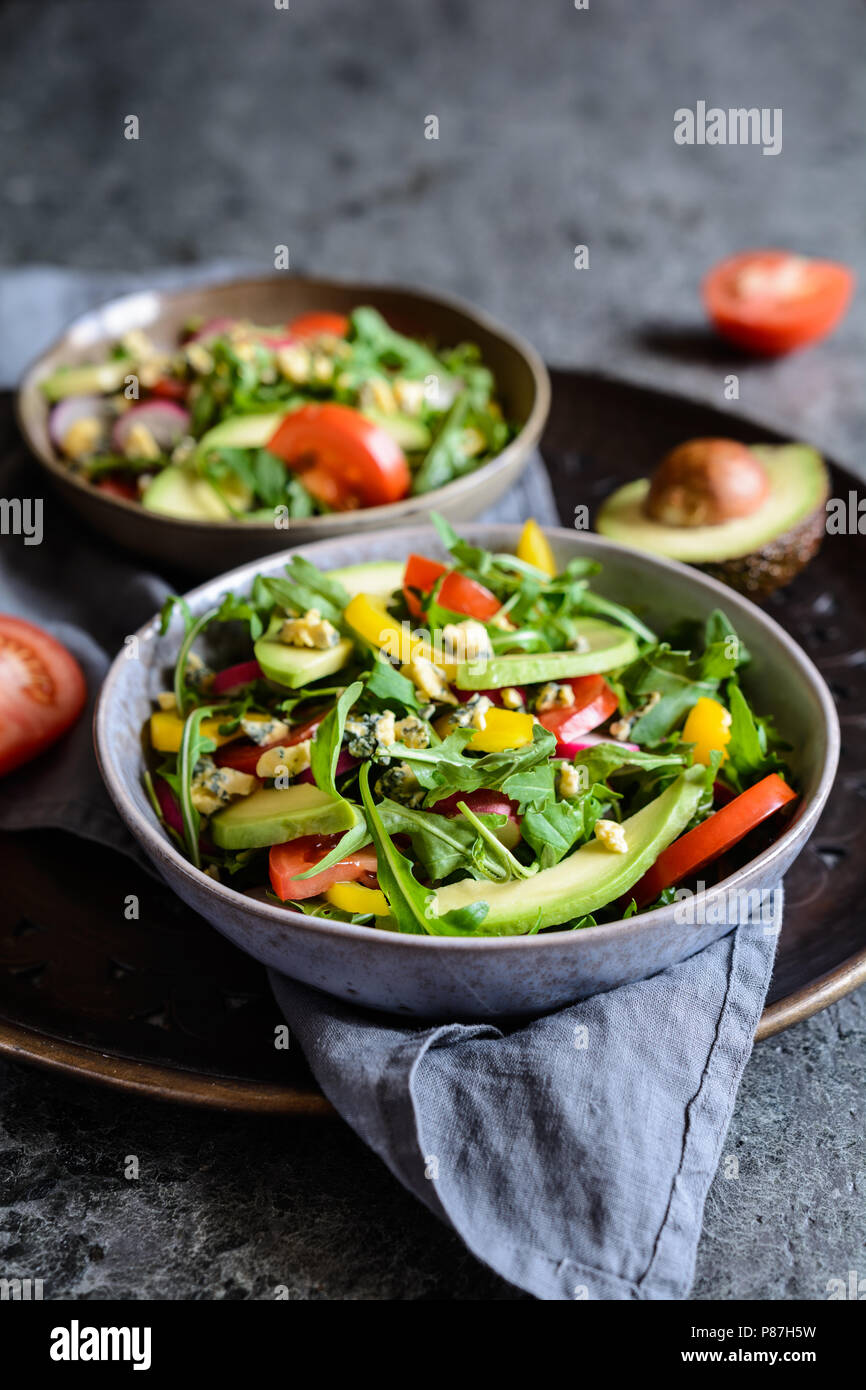 Matières premières en bonne santé avec de l'avocat salade de roquette, radis, poivrons, tomates et fromage de Roquefort Banque D'Images