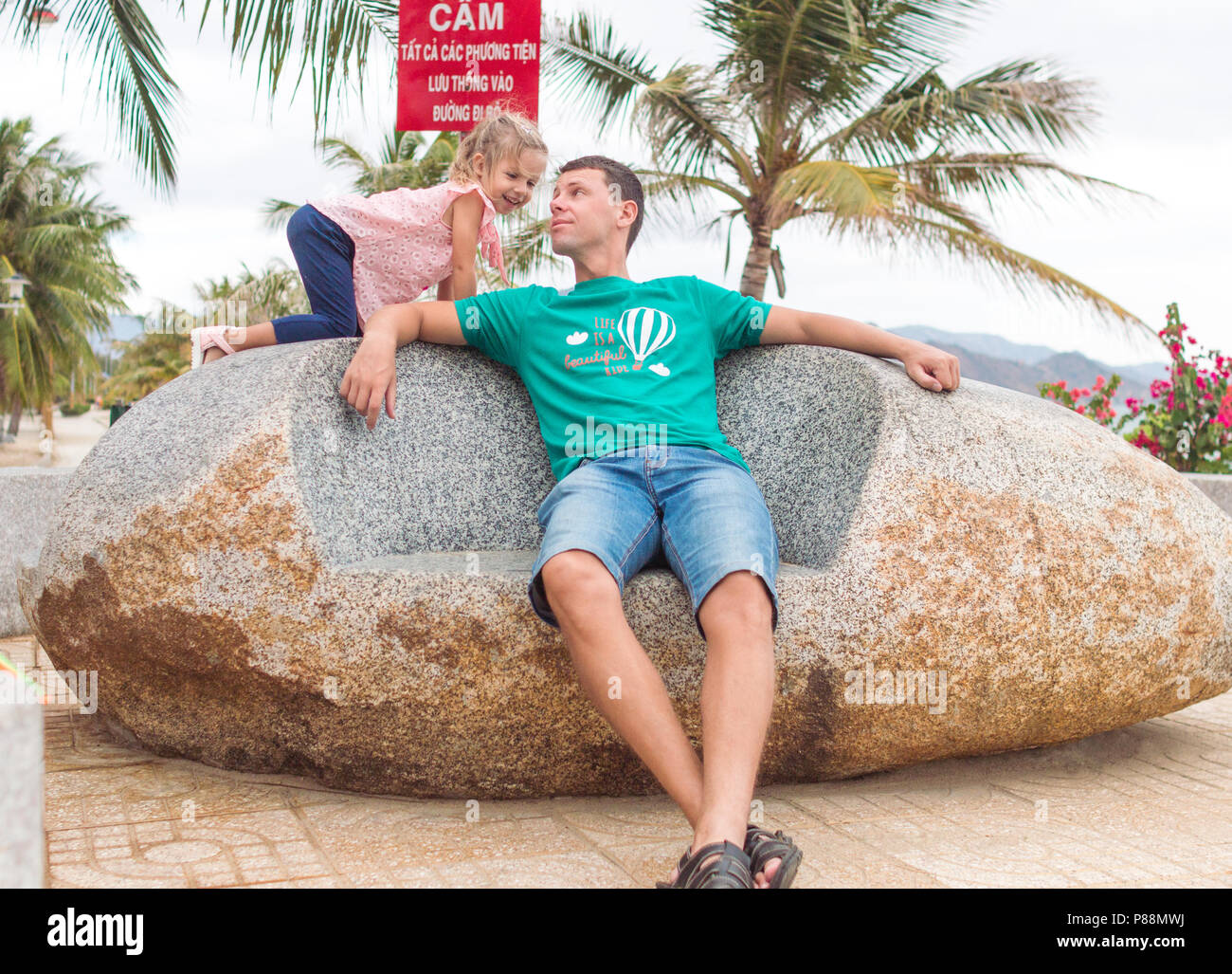 Heureux père d'un enfant assis sur la pierre près de la plage, ils jouent et sourire. Banque D'Images