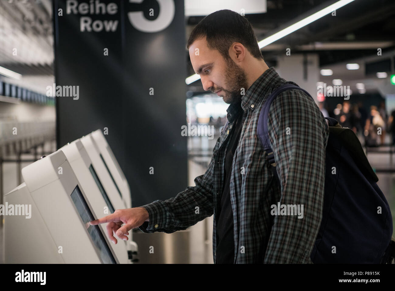 Jeune homme sac à dos avec l'aide d'affichage interactif touchant machine self-service, faire l'enregistrement en cas de vol ou d'acheter des billets d'avion à dispositif automatique dans l'aérogare moderne Banque D'Images