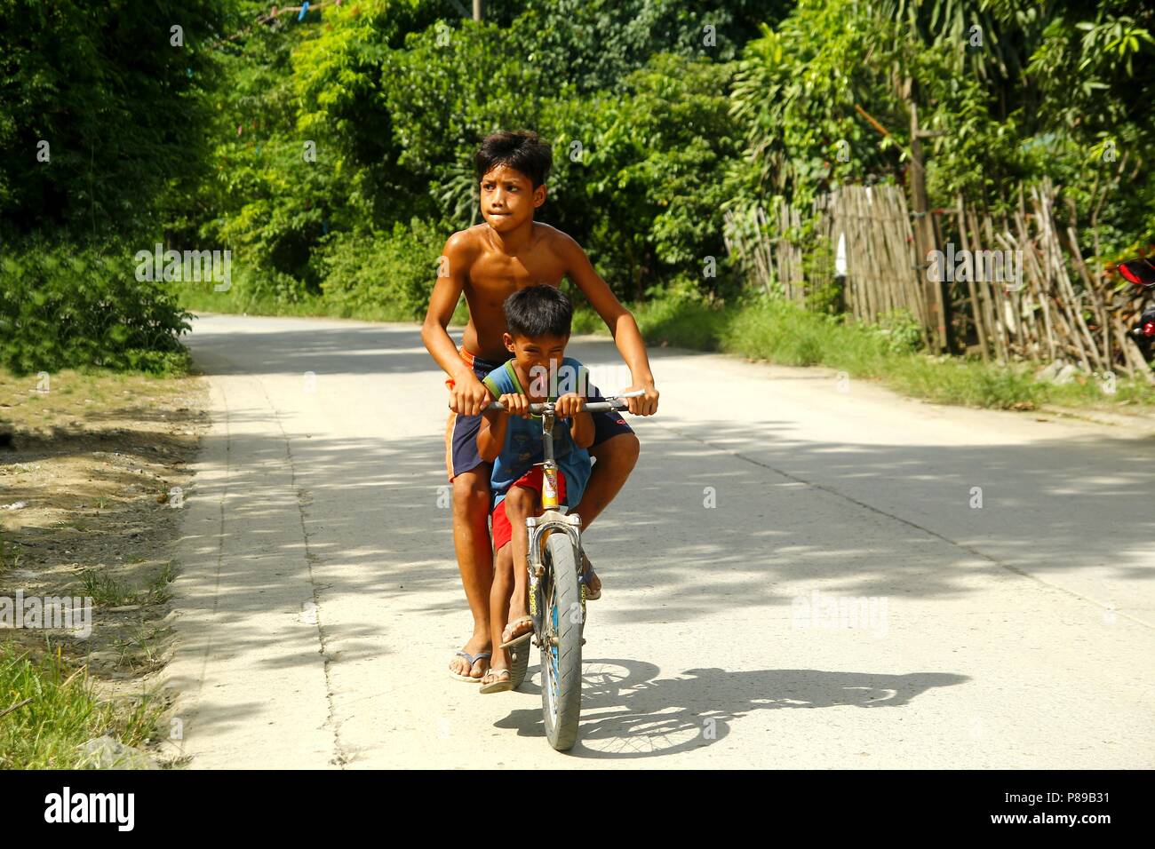 ANGONO, Rizal, PHILIPPINES - le 4 juillet 2018 : les jeunes enfants philippins jouer et faire du vélo le long d'une rue. Banque D'Images