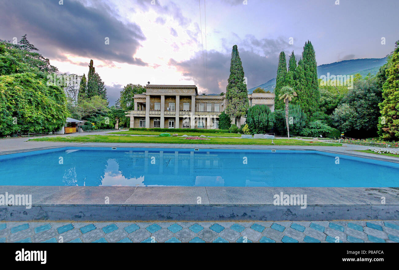 Lumière chic villa de deux étages avec une pelouse, une grande piscine bleu entouré de grands arbres verts sur fond de montagnes et le sombre ciel. pl Banque D'Images