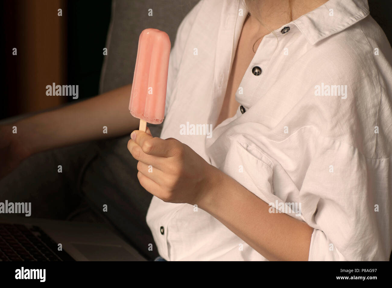 Young woman eating ice cream en utilisant un ordinateur portable. Les femmes travaillant sur ordinateur portable dans une piscine en plein air, assis sur le canapé à la maison Banque D'Images