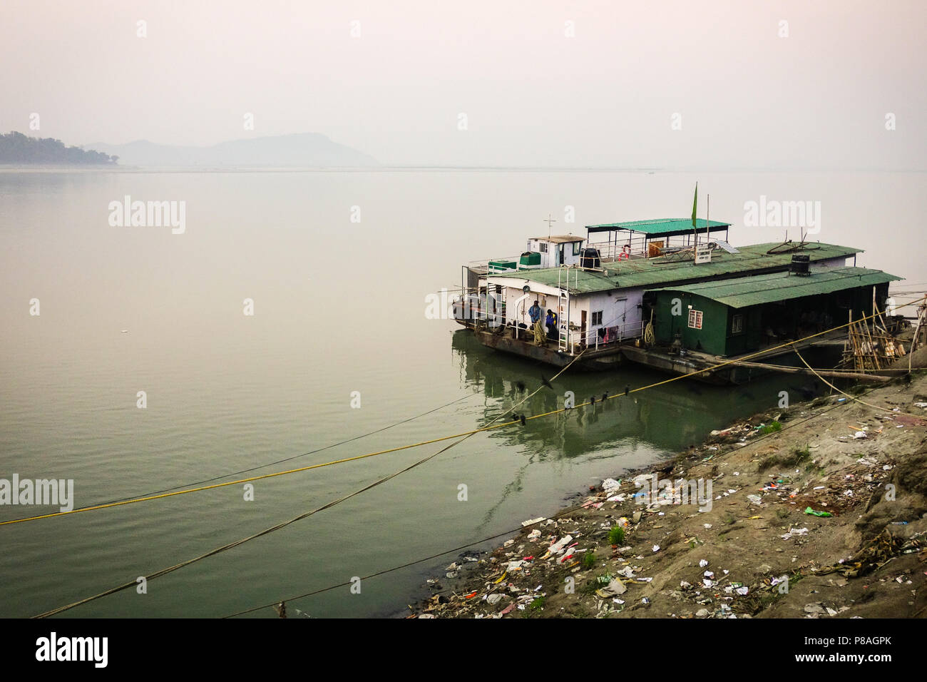 Belle vue sur le Brahmapoutre avec croisière bateau ancré à la terre polluée en plastique à Guwahati, Assam, Inde. Banque D'Images