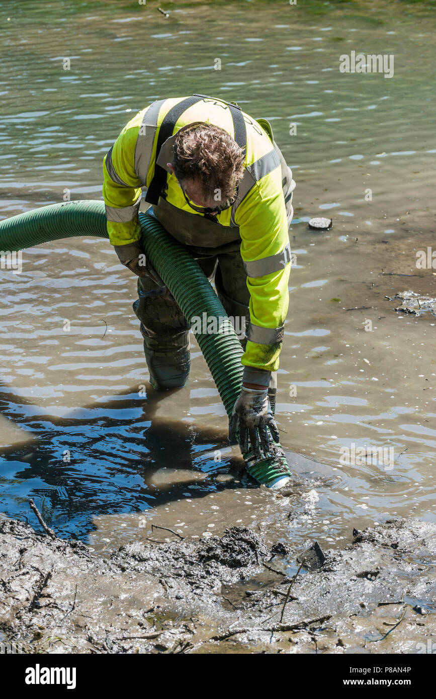 Un travailleur à l'aide d'une pompe d'aspiration pour enlever la boue et la vase dans un lac. Banque D'Images