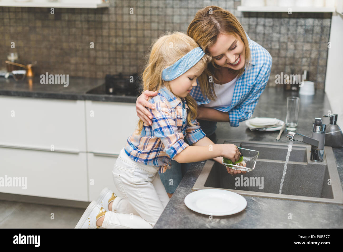 Vue de côté de fille mère aidant à faire la vaisselle après le dîner à la maison Banque D'Images