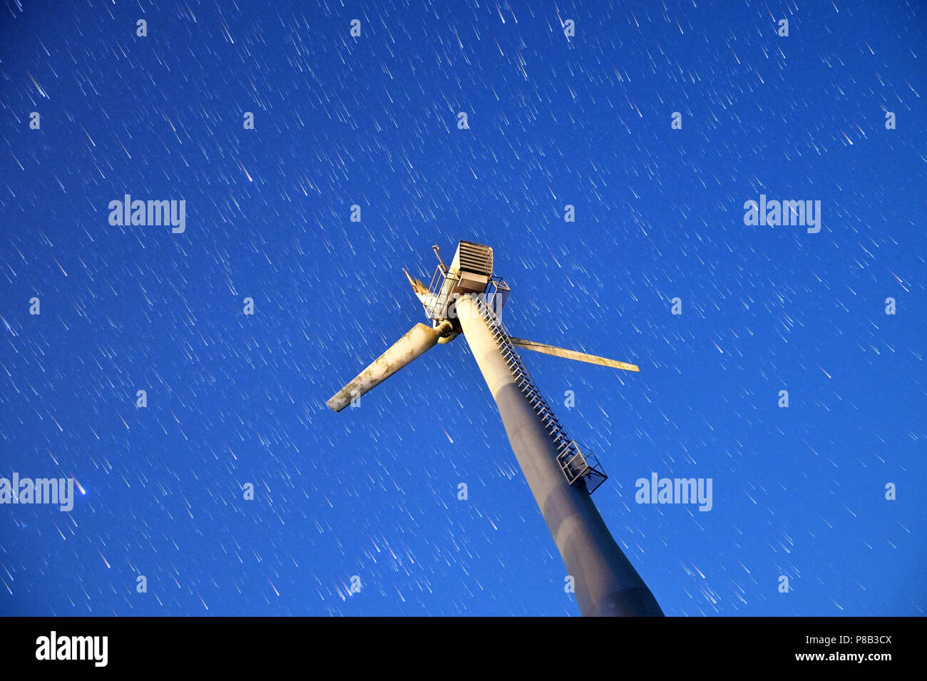 Vue de dessous d'une lame endommagée trois wind turbine moulin sur bleu clair ciel nocturne avec star trails. Banque D'Images